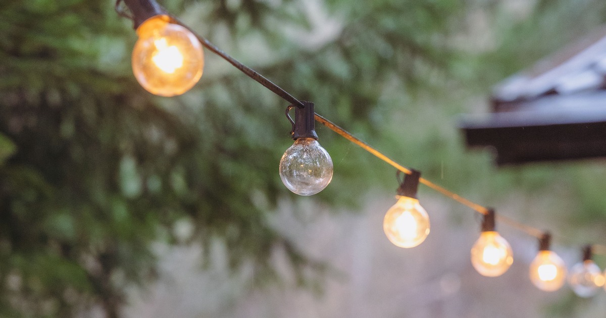 Prikkabel met losse lampen tussen bomen en terras