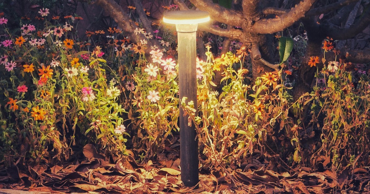 Lage staande buitenlamp bij een pad en bloeiende beplanting